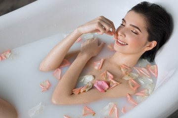 Young woman getting spa treatment at beauty salon. Pleased relaxing brunette female with white fresh skin closes eyes enjoying in milky aroma water with petals bath.