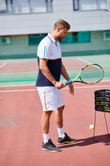 Tennis male player. Handsome bearded sportsman standing with racket on outdoor red clay court.