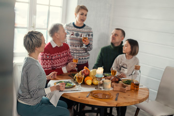 young fair-haired beautiful woman holding a glass and talking soething to her relatives. blurred image