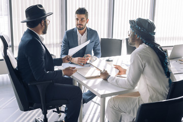 Multiracial group of confident focused experts is analyzing business result sitting at table in Customer modern office in the Middle East