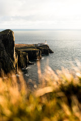 Sunset at Neist Point Lighthouse at the coastline of Skye with grass foreground and sunny sky (Isle of Skye, Scotland, United Kingdom, Europe)