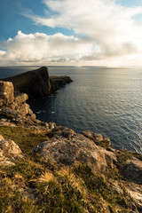 Fototapeta na wymiar Sunset at Neist Point Lighthouse with rocky shore, dramatic sky and sun bursting through clouds before sunset (Isle of Skye, Scotland, Europe)