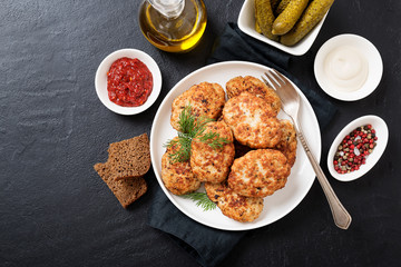 Juicy delicious meat cutlets in a white plate on a black stone table. Top view 