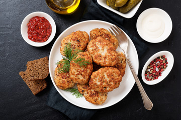 Juicy delicious meat cutlets in a white plate on a black stone table. Top view 