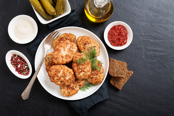 Juicy delicious meat cutlets in a white plate on a black stone table. Top view 