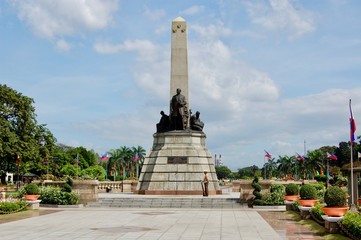 Rizal Park in downtown Manila on a beautiful day with blue sky and clouds looking towards the sculpture, park, and the Philippines Flag
