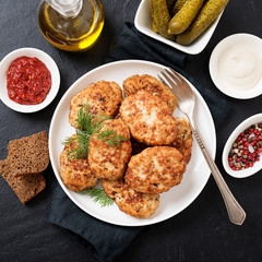 Juicy delicious meat cutlets in a white plate on a black stone table. Top view 