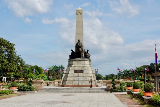 Rizal Park in downtown Manila on a beautiful day with blue sky and clouds looking towards the sculpture, park, and the Philippines Flag