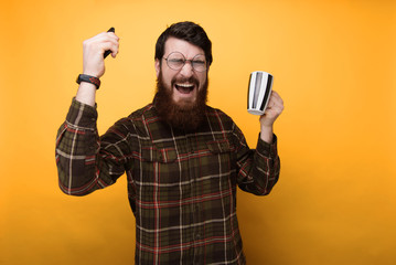 Portrait of bearded man smiling at the friends joke while drinking coffee over yellow background