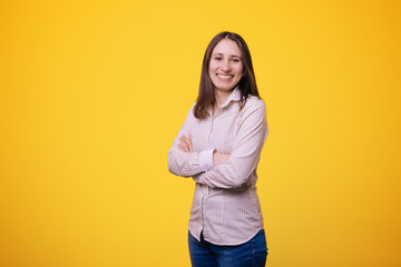 Smiling business woman with folded hands against yellow background. Toothy smile, crossed arms