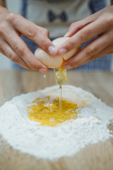 The girl is ruining the egg with his hand, preparing the dough for homemade noodles.