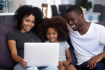 Happy african american family with child girl having fun using laptop together at home, black parents and little kid daughter watch funny video, do online shopping, make call look at computer screen