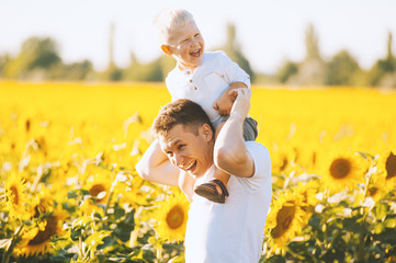 Picture of father with little boy sitting on his father shoulders in field of blooming sunflower Fahter having fun with child