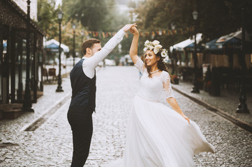 Beautiful newlywed couple is having fun while dancing in the sunny old town street
