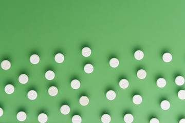 White pills on green background with deep shadows. Flat lay.