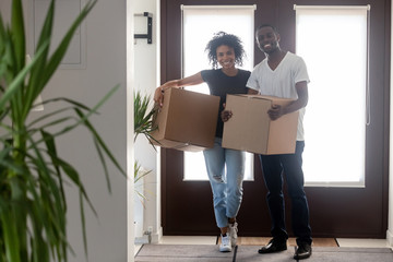 Black couple holding boxes standing in hallway looking at camera, african renters tenants first time buyers relocate into new house, happy home owners on moving day portrait, family mortgage goals
