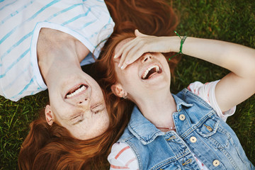 Friendship is miracle. Joyful and carefree cute redhead girls with freckles, lying on green grass...