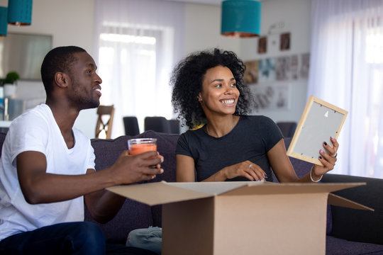 Happy african couple having fun unpacking in living room on moving day, black tenants talking unboxing cardboard boxes discussing renovation decor ideas, packing, relocation into new home concept