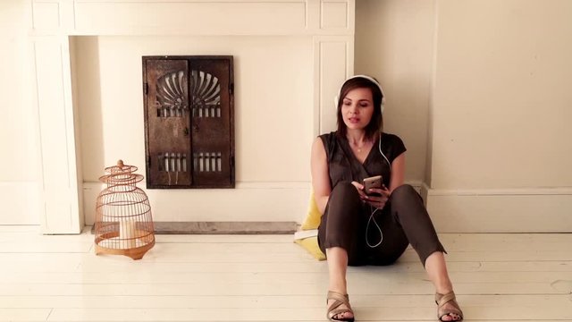 Happy woman listening music sitting on the floor at home
