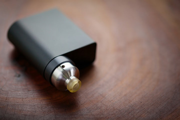 high end rebuildable dripping atomizer with black regulated box mods on wood texture background,...