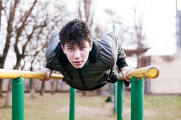 Fototapeta premium A teen in the spring doing physical exercises on the street near his school. The guy is pushing up on the bars