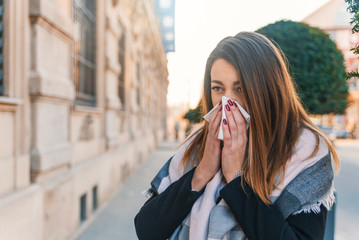 Seasonal virus infection. Sick young woman with seasonal influenza blowing her nose on a tissue. Woman has sneezing. This flu is getting to her. Young woman coughing covering her mouth with a tissue