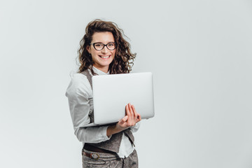 Naklejka premium BBeautiful young girl smiles. Works on a laptop in glasses and a white shirt
