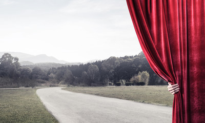 Countryside road behind red curtain and hand holding it