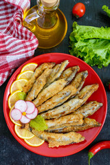Fried capelin with lemon on a red plate on a black wooden background. A dish of small sea fish. Top view. Flat lay
