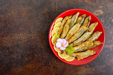 Fried capelin with lemon on a red plate. A dish of small sea fish. Top view. Flat lay