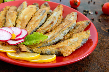 Fried capelin with lemon on a red plate. A dish of small sea fish.