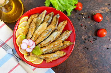 Fried capelin with lemon on a red plate. A dish of small sea fish. Top view. Flat lay