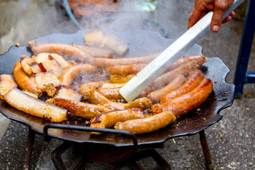 Turning delicious juicy sausages on barbecue plate with handle.