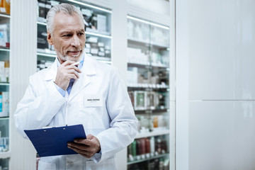 Fototapeta premium Grey-haired bearded pharmacist in a blue shirt comparing medicines