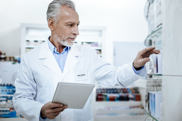 Grey-haired handsome pharmacist in a white coat making notes