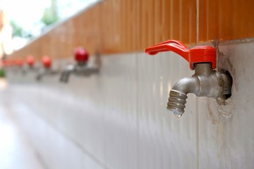 Focus on faucet is not compleately closed in foreground with blurred row of steel taps in water supply at school, close up and perspective view