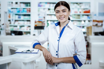 Dark-haired beaming young woman in a white coat smiling bright