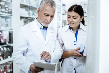 Mature bearded man in a white coat discussing medicines with his young colleague