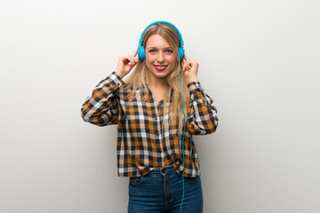 Blonde young girl over white wall listening to music with headphones