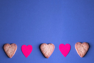 Heart-shaped gingerbread and paper hearts on blue-gray background. Top view