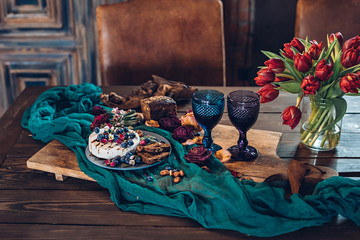 Food composition on wooden table with camembert cheese, balsamic sauce, blueberries, tulips and two glasses with red wine