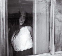 girl by the window in a wooden house with dim light black and white colors