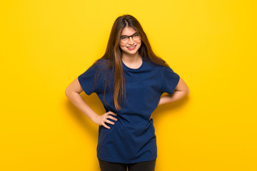 Young woman with glasses over yellow wall happy and smiling