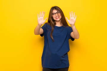 Young woman with glasses over yellow wall counting ten with fingers