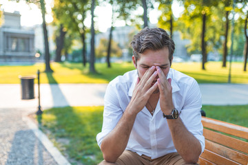 Closeup portrait, stressed young business man, hands on head with bad headache, isolated background of trees outside. Negative human emotion facial expression feelings.