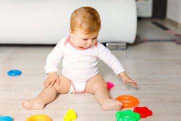Adorable baby girl playing with educational toys in nursery. Happy healthy child having fun with colorful different toys at home. Kid trying to build plastic pyramid and using blocks with letters