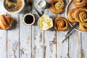 Variety of homemade puff pastry buns cinnamon rolls and croissant served with coffee cup, jam,...