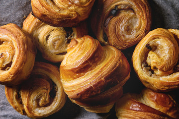 Variety of homemade puff pastry buns cinnamon rolls and croissant over grey cloth. Flat lay, cloth up - obrazy, fototapety, plakaty