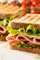 Close-up photo of a club sandwich. Sandwich with meat, prosciutto, salami, salad, vegetables, lettuce, tomato, onion and mustard on a fresh sliced rye bread on wooden background. Olives background.