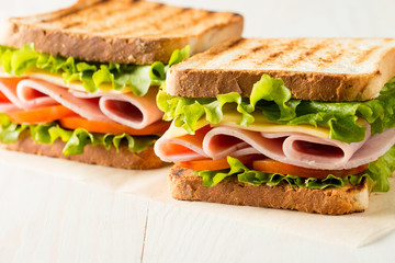 Close-up photo of a club sandwich. Sandwich with meat, prosciutto, salami, salad, vegetables, lettuce, tomato, onion and mustard on a fresh sliced rye bread on wooden background. Olives background.